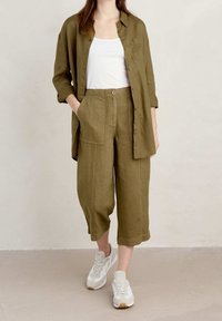 Lightweight olive green linen shirt with a pocket, paired with matching cropped linen trousers. The outfit is complemented by white sneakers.