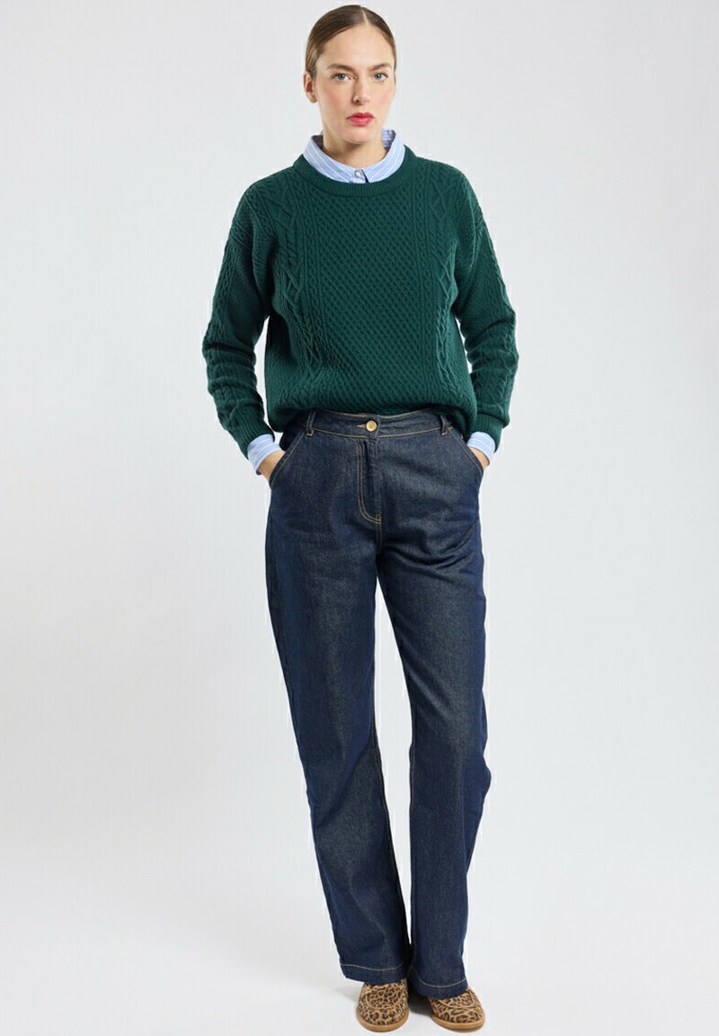 Groene kabelgebreide trui met ronde hals, gecombineerd met hoge, donkerblauwe jeans. Bevat een blauwe overhemd eronder en schoenen met een luipaardprint.