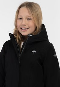 Svart jacka med dragkedja framtill, grå innerfoder och en paraplylogotyp. Har en huva och kardborreaccent på kragen och fickorna.