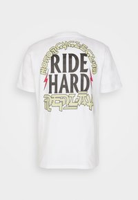 Camiseta de algodón blanca con el texto en bold negro "RIDE HARD", rodeado de acentos amarillos y rojos, y diseño gráfico en la parte de atrás.