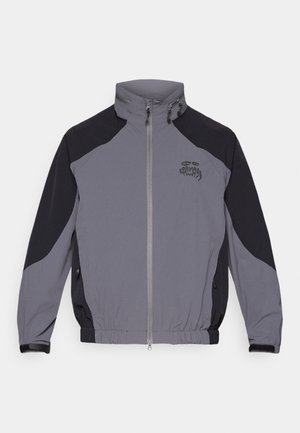 Casaco corta-vento cinza e preto com colarinho alto, fecho com zipper e punhos elásticos. Apresenta um logótipo no peito e bolsos laterais.