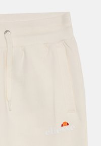 Kremaste joggerice s rebrastim pojasom, uzicom, bočnim džepovima i otisnutim "ellesse" logotipom s šarenom obodom.