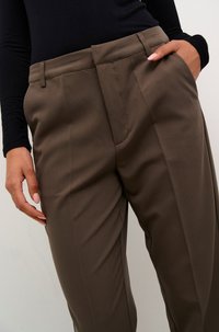 Pantalons marron sur mesure avec une texture lisse, dotés de poches latérales, d'une coupe droite et de plis marqués à l'avant. Portés avec un haut noir à manches longues.