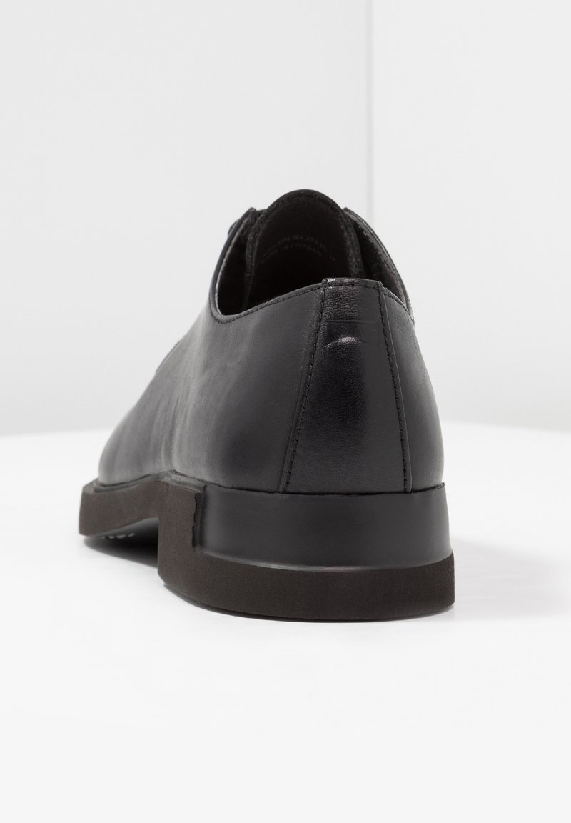 Schwarzer Lederschuh mit glatter Oberfläche, abgerundetem Design und einer flachen Gummisohle. Verfügt über einen subtilen Absatz und minimale Nähte.