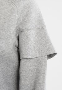 Szara bluza z krótkimi, złożonymi rękawami. Miękka tekstura, dzianinowy materiał, z dyskretnymi detalami w szyciu. Prosty, casualowy design.