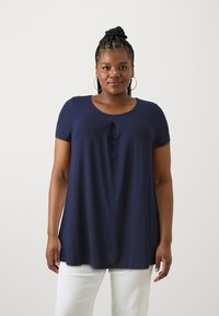 Navyblauw kortemouwenshirt met een ronde halslijn en een kleine knoopdetail in het midden. Zacht materiaal met een comfortabele pasvorm, gecombineerd met witte broeken.