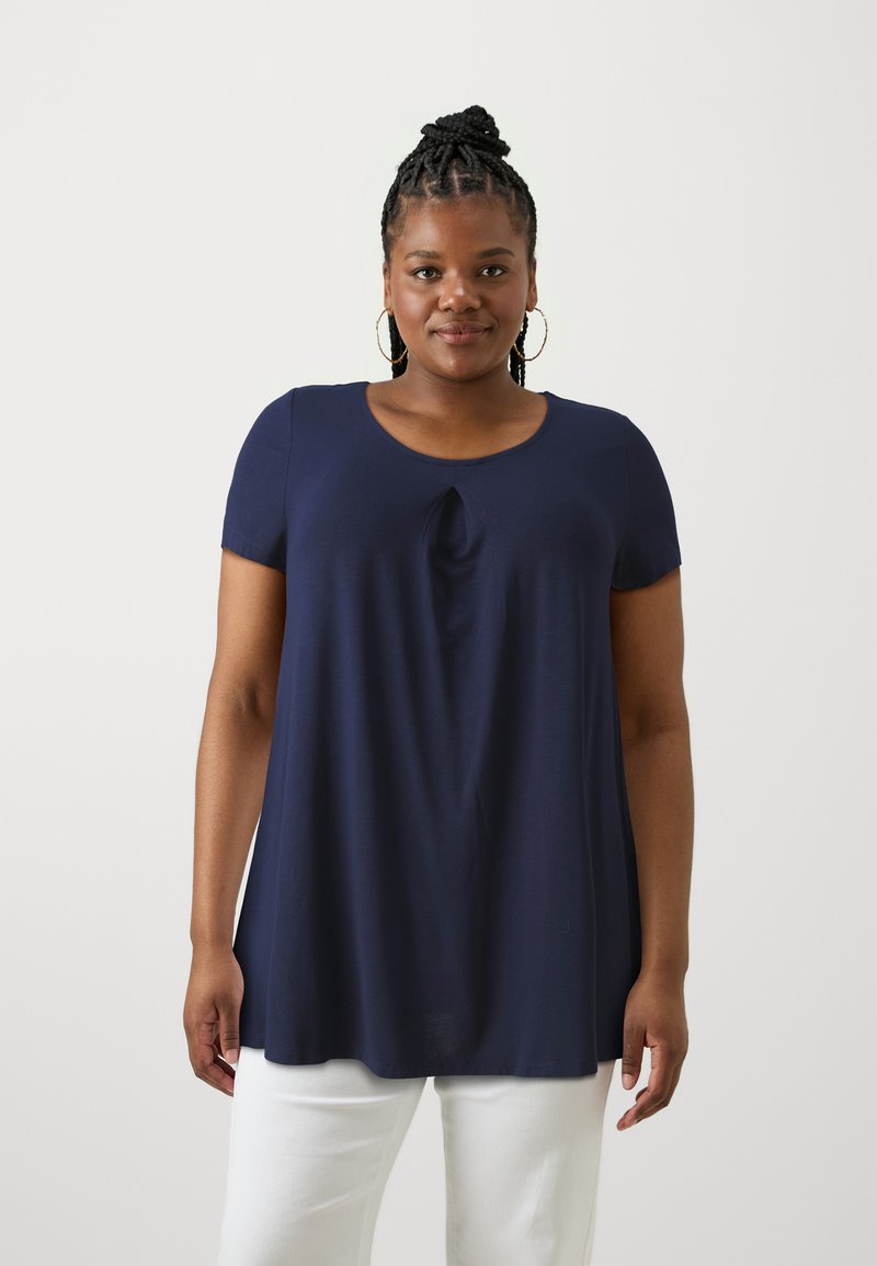 Navyblauw kortemouwenshirt met een ronde halslijn en een kleine knoopdetail in het midden. Zacht materiaal met een comfortabele pasvorm, gecombineerd met witte broeken.