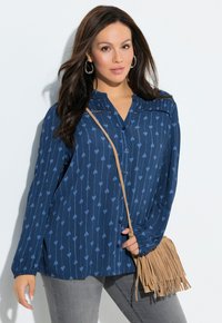 Marineblauw overhemd met knopen, een hartjespatroon, lange mouwen en een geplooide achterkant. Gecombineerd met een beige handtas met franjes.