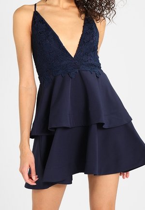 Granatowa sukienka z głębokim dekoltem w kształcie litery V ozdobionym koronką oraz wielowarstwową spódnicą. Lekki materiał o zwiewnej fakturze i regulowanych ramiączkach.