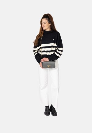 Maglione a righe bianco e nero con colletto alto, abbinato a pantaloni bianchi alla moda e mocassini platform neri. Tiene in mano una borsa a tracolla grigia.