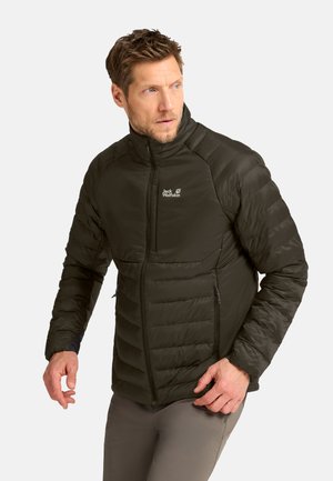 Uomo che indossa una giacca imbottita verde scuro con zip e logo, guarda di lato su uno sfondo chiaro e uniforme.