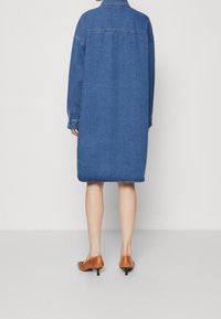 Denim shirt dress in dark blue with a relaxed fit, long sleeves, and a rounded hem. Accented with button closures and stitched details.