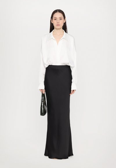 White silk shirt with a loose fit, paired with a long black skirt in smooth fabric. A small black crocodile-patterned handbag is held.