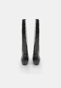 Bottes noires en cuir verni jusqu'aux genoux avec un motif crocodile, présentant un bout carré et un talon épais, conçues pour une silhouette élégante.