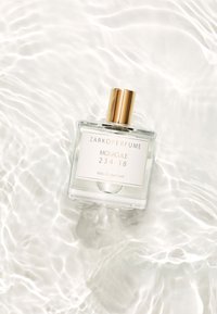 Genomskinlig glasparfymflaska med ett guldock, märkt "ZARKOPERFUME MOLECULE 234:38 eau de parfum", placerad på en yta av vågigt vatten.