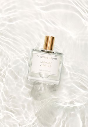 Clear glass perfume bottle featuring a gold cap, labeled "ZARKOPERFUME MOLECULE 234:38 eau de parfum," placed on rippled water surface.