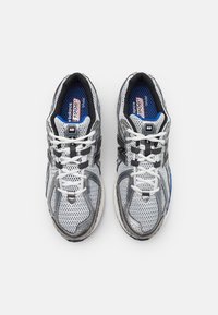 Ett par vita och grå nätlöparskor från New Balance med svarta och blå accenter, vita snörning och blå innersulor som visar varumärke och modellinformation.