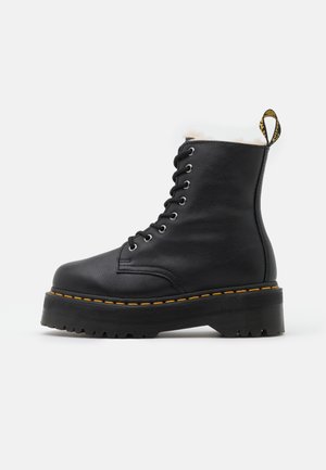 Botte en cuir noir avec une tige haute, fermeture à lacets à l'avant, doublure en fourrure sur le haut, couture jaune, et semelle plateforme robuste.