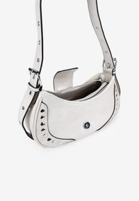 Bolso de mano de cuero blanco con una forma curva, detalles de tachuelas a lo largo del costado y una correa desmontable. Cuenta con un compartimento principal con cremallera.