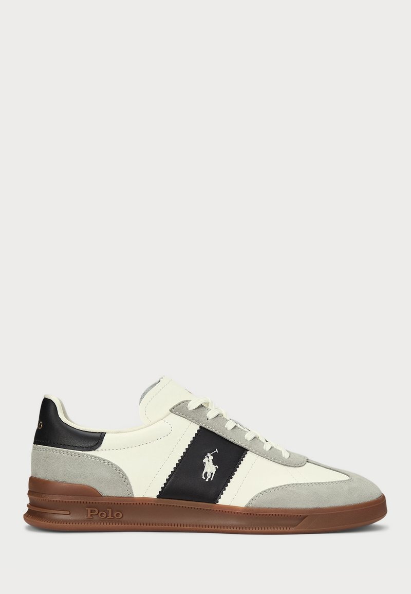Baskets basses avec des panneaux en suède blanc, gris et cuir noir, avec le logo Polo et une semelle en caoutchouc marron.