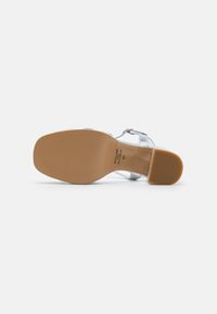 Sandal con tacco argento e design con cinturino trasparente. Presenta una suola liscia e opaca color beige con una superficie testurizzata e un piccolo tacco a blocco.