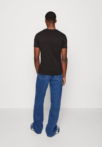 Black short-sleeve t-shirt with a round neckline, paired with loose blue denim jeans, seen from the back against a plain background.
