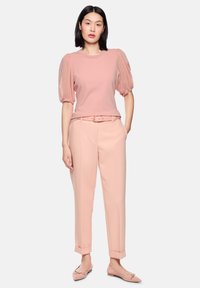 Light pink top with puffed sheer sleeves paired with structured light pink trousers, tailored fit, and matching flats. Soft fabric texture.