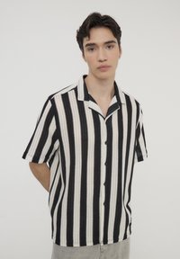 Camicia a maniche corte con colletto, a righe verticali bianche e nere, caratterizzata da una chiusura a bottoni e un tessuto testurizzato.