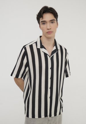 Camicia a maniche corte con colletto, a righe verticali bianche e nere, caratterizzata da una chiusura a bottoni e un tessuto testurizzato.