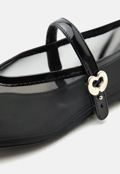 Μαύρο πλεκτό Mary Jane flat παπούτσι με λουρί λάκας και κούμπωμα καρδιάς από χρυσό σε λευκό φόντο.