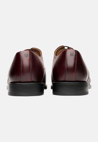 Scarpe in pelle bordeaux con finitura liscia, tacco arrotondato, dettagli di cucitura minimi e suola nera. Logo sottile impresso sul tacco.