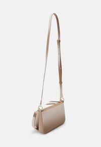 Petit sac bandoulière beige avec sangle réglable et détails de fermeture éclair dorée, présenté sur fond blanc uni.