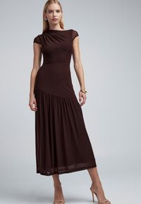 Smeđa, uska duga haljina s kratkim rukavima, detalj skupljen sa strane, lepršava suknja, izrađena od mekanog tkanja. Naglašena minimalističkim dodacima.