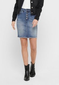 Jeanskjol i medelblått med fransad nederkant och sexknappslås framtill. Bärs med svarta ankelskór och en vit top.