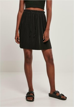 Jupe plissée noire avec une taille élastique et un cordon de serrage, associée à des sandales noires à enfiler. Design simple avec un tissu texturé.