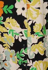 Blumenmusterstoff mit schwarzem Hintergrund; zeigt leuchtende Grüntöne, Gelb und Orange. Enthält schwarze Knöpfe entlang der Front.
