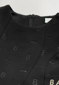 Schwarz Kleidungsstück aus strukturiertem Stoff, mit einem geprägten Design von Buchstaben "B" und einem Fliegenmuster, sowie einem Etikett im Inneren.