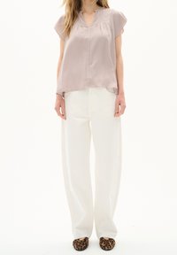 Blusa mauve chiaro con scollatura a V e pieghe, abbinata a pantaloni bianchi a gamba larga e ballerine con stampa leopardata. Tessuto morbido, design casual.