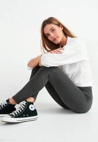 Sive tajice od rastezljivog materijala, uparene s crnim tenisicama do gležnja s bijelim detaljima. Outfit upotpunjuje bijela majica.