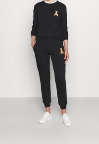 Svart sweatshirts och sweatpants-set gjort av mjukt tyg, med guldbi-broderi på bröstet och låret; parat med vita sneakers.