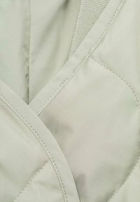 Tessuto grigio chiaro trapuntato con una texture liscia, caratterizzato da cuciture diagonali e un bordo a contrasto lungo il margine.