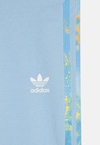 Adidas lichtblauwe sportbroek met bloemenpatroon op de zijkanten en een wit logo. De stof lijkt zacht met een gladde textuur.