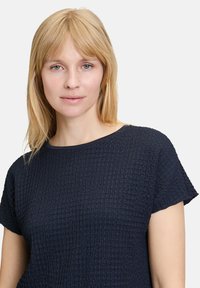Top in blu navy con texture, maniche corte e scollatura rotonda. Presenta un motivo di tessuto stropicciato e bordi lisci.