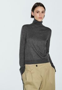 Maglione grigio a collo alto realizzato in materiale morbido, con una vestibilità aderente e polsini a costine, abbinato a pantaloni beige a vita alta con pieghe.