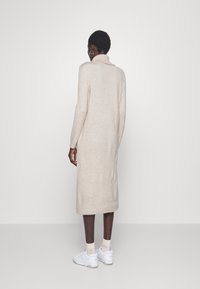 Vestito in maglia beige con colletto a imbuto, maniche lunghe e orlo a costine. Indossato con sneakers bianche e calzini alla caviglia.