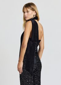 Schwarzes ärmelloses Oberteil aus Wildleder mit hohem Kragen und einer Rückenschnürung, kombiniert mit schwarzen Hosen mit Paillettenbesatz. Glatte Textur durchgehend.