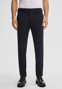 Pantaloni tailored blu navy realizzati in un tessuto liscio e testurizzato, con tasche frontali e passanti per la cintura; abbinati a scarpe nere con lacci.