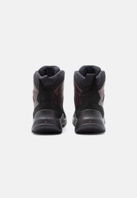 Mustade ja pruunide kõrgete matkasaabaste paar, shown taga poolt valgel taustal, kannatõmbemärgistega kanna peal.