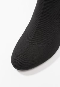 Bottine en tricot noir avec un bout rond, une texture côtelée et un design sans couture. Le matériau semble extensible et moulant.