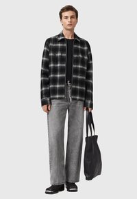 Camicia di flanella a scacchi in bianco e nero con due tasche sul petto, abbinata a jeans grigi a vita alta e borsa nera. Tessuto morbido, vestibilità rilassata.
